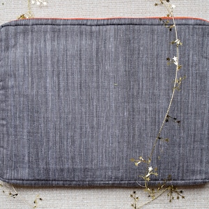 May include: A gray laptop sleeve with an orange zipper and a subtle textured fabric. The sleeve is surrounded by a gold garland of stars.