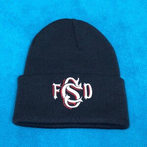 Puede incluir: Un gorro de punto negro con un logotipo bordado en blanco que dice "FSD" en una fuente estilizada.