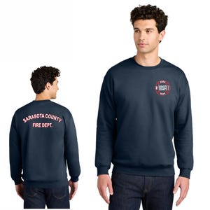 Puede incluir: Una sudadera azul marino con un logotipo rojo y blanco en el lado derecho que dice "Fire Sarasota County Dept." y el texto "Sarasota County Fire Dept." en la parte posterior en rosa.