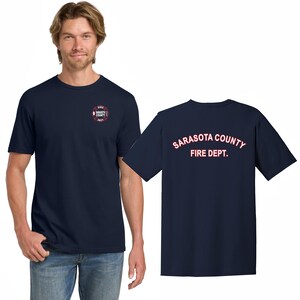 Puede incluir: Una camiseta azul marino con un logotipo rojo y blanco en el pecho izquierdo y el texto "SARASOTA COUNTY FIRE DEPT." en rojo en la espalda.