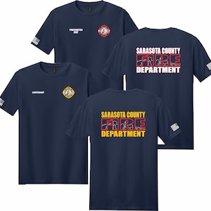 Puede incluir: Camisetas de manga corta azul marino con el logotipo del Departamento de Bomberos del Condado de Sarasota. El frente muestra insignias con textos como Firefighter EMT o Lieutenant. La espalda presenta el nombre en rojo o amarillo con un gráfico.