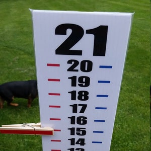 May include: A white vertical height chart featuring black numbers from 0 to 21, with red tick marks on the left and blue tick marks on the right. Two wooden clothespins, one red and one blue, are clipped to the chart. Text reads: Stand is NOT included.