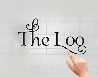 May include: Black cursive text that reads "The Log" with a decorative flourish. A hand is pointing at the word "Log". The background is a blurred white and gray.