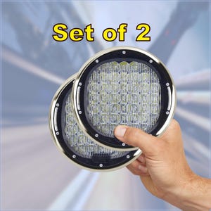 May include: Set of two round, white LED lights with a black trim and a silver outer ring. The lights are held in a hand.