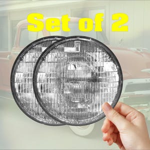 May include: A set of two round, clear glass automotive headlights featuring a textured, multi-faceted reflector pattern. The lenses are circular with a black rim and include the text Set of 2 displayed in yellow above the headlights.