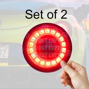 May include: Set of two red round LED tail lights with a ring of lights around the center. The lights are held in a hand.