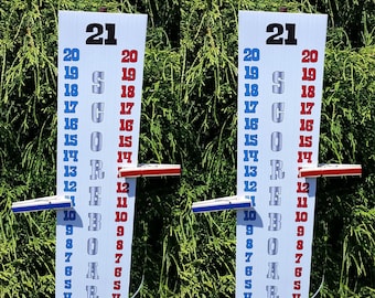 May include: Two white wooden scoreboards with blue and red sliding pieces. The scoreboards are numbered 4 to 21 and have the word "SCORE" written vertically in silver letters.