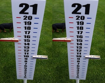 May include: A white vertical score tracker sign featuring black numbers from 21 down to 0, with alternating red and blue horizontal dash marks. Two wooden clothespins are attached to the sign, one red on the left at 15 and one blue on the right at 10.