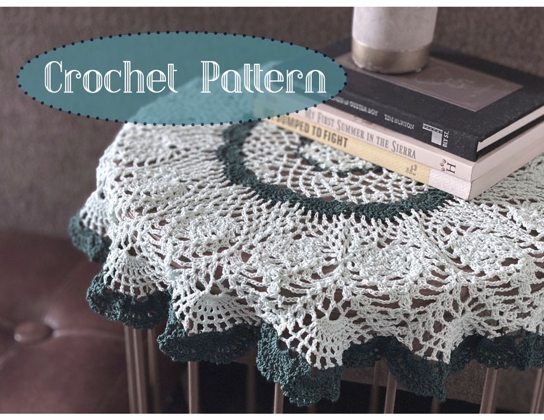 May include: A crocheted doily in white and green with a scalloped edge. The doily is on a small table with books stacked on top.