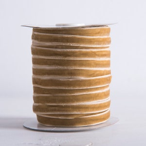 May include: A spool of gold velvet ribbon with a white backing. The ribbon is wound tightly around the spool.