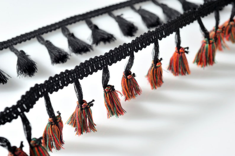 以下が含まれることがあります： 黒とマルチカラーのタッセルトリムで、黒い織り地ベース。タッセルは柔らかく、質感のある糸で作られています。