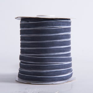 May include: A spool of grey velvet ribbon. The ribbon is wound tightly around the spool and has a subtle sheen.
