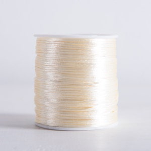 Può includere: Un'bobina di filo color crema avvolto su una bobina di plastica bianca.
