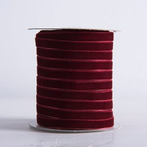 May include: A spool of burgundy velvet ribbon. The ribbon is wound tightly around the spool and is ready to be used for crafting or decorating.