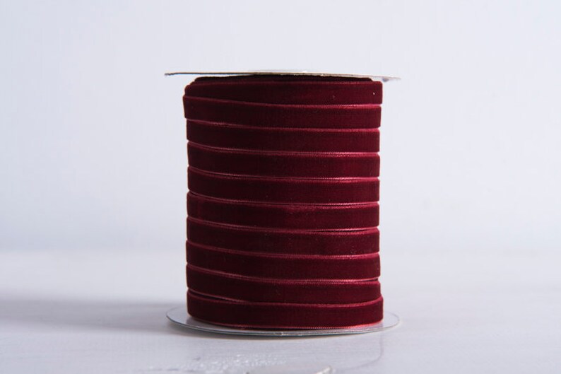 Może przedstawiać: Szpula z burgundową wstążką welurową. Wstążka jest ciasno nawinięta na szpulę i gotowa do użycia do rękodzieła lub dekoracji.