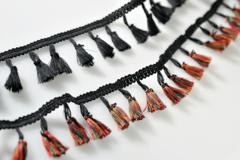 以下が含まれることがあります： 黒とマルチカラーのタッセルトリムで、織り込まれたコードベースが付いています。トリムにはタッセルの列が2列あり、1列は黒いタッセル、もう1列はマルチカラーのタッセルです。