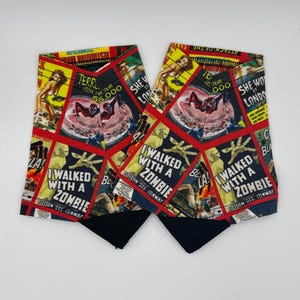 May include: A pair of black and red fabric wrist cuffs with a collage of vintage horror movie posters. The posters feature images of monsters, creatures, and people in danger. The text on the posters includes "I Walked With A Zombie" and "She-Wolf of London".