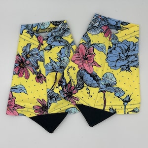 May include: A pair of yellow floral boot cuffs with black trim. The cuffs feature a floral pattern with pink, blue, and green flowers on a yellow background with white polka dots.