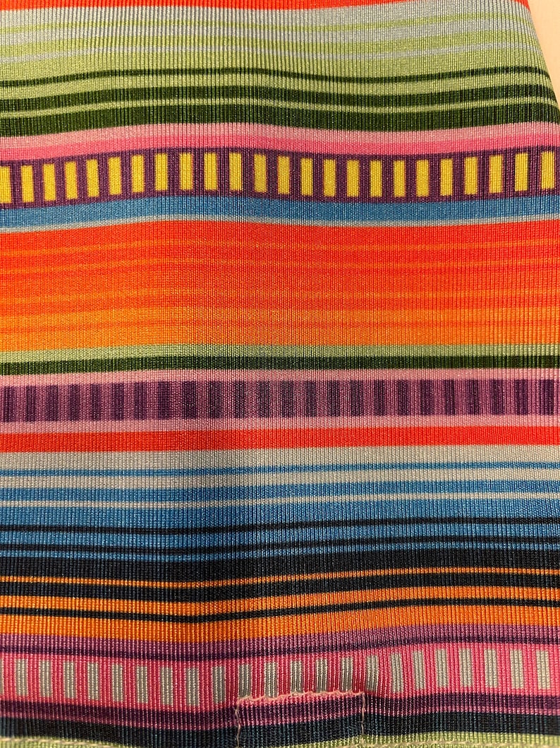 K&ouml;nnte beinhalten: Bunt gestreiftes Gewebe mit einer Vielzahl von Farben, darunter Orange, Gr&uuml;n, Blau, Rosa und Schwarz.