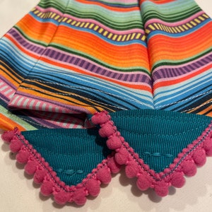 K&ouml;nnte beinhalten: Zwei t&uuml;rkisfarbene Stoff-Haarband mit rosa Bommelbesatz. Die Haarband haben ein buntes Streifenmuster.