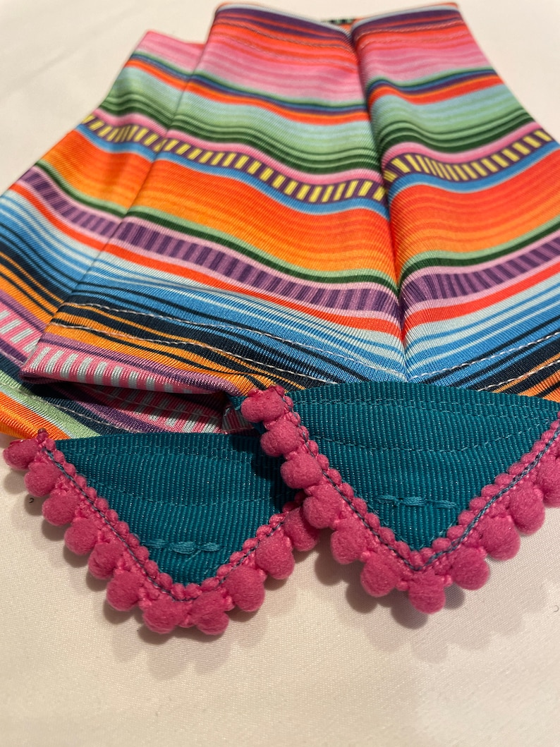 K&ouml;nnte beinhalten: Zwei t&uuml;rkisfarbene Stoff-Haarband mit rosa Bommelbesatz. Die Haarband haben ein buntes Streifenmuster.