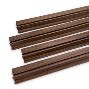 May include: Several dark brown wooden picture frame rails with a grooved design. The rails are angled and appear to be made of a solid wood material. The grooves run the length of the rails.