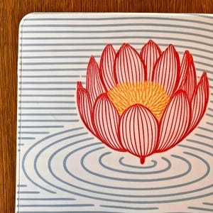 以下が含まれることがあります： 赤い蓮の花と黄色の中心、詳細な線が特徴の長方形のマウスパッド。 デザインは、水色の水平ストライプと同心円の背景に配置され、穏やかなデザインを作り出しています。