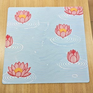 以下が含まれることがあります： 赤と黄色の蓮の花と、同心円状のさざ波模様が繰り返される、正方形の薄い青色のマウスパッド。マウスパッドには白い縁取りがあり、右下隅に「Pillow Friends」の文字が入っています。