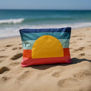 May include: A colorful beach bag with a sunset design. The bag features horizontal stripes in shades of blue, teal, and orange, with a large yellow sun graphic. The bag is made of a lightweight material and has a white zipper.