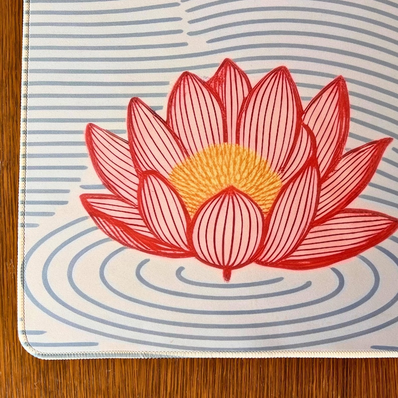 以下が含まれることがあります： 赤い蓮の花と黄色の中心部が特徴のフローラルデザイン。背景は青い水平線と同心円。デザインは白い表面にあり、背景は木製の表面です。