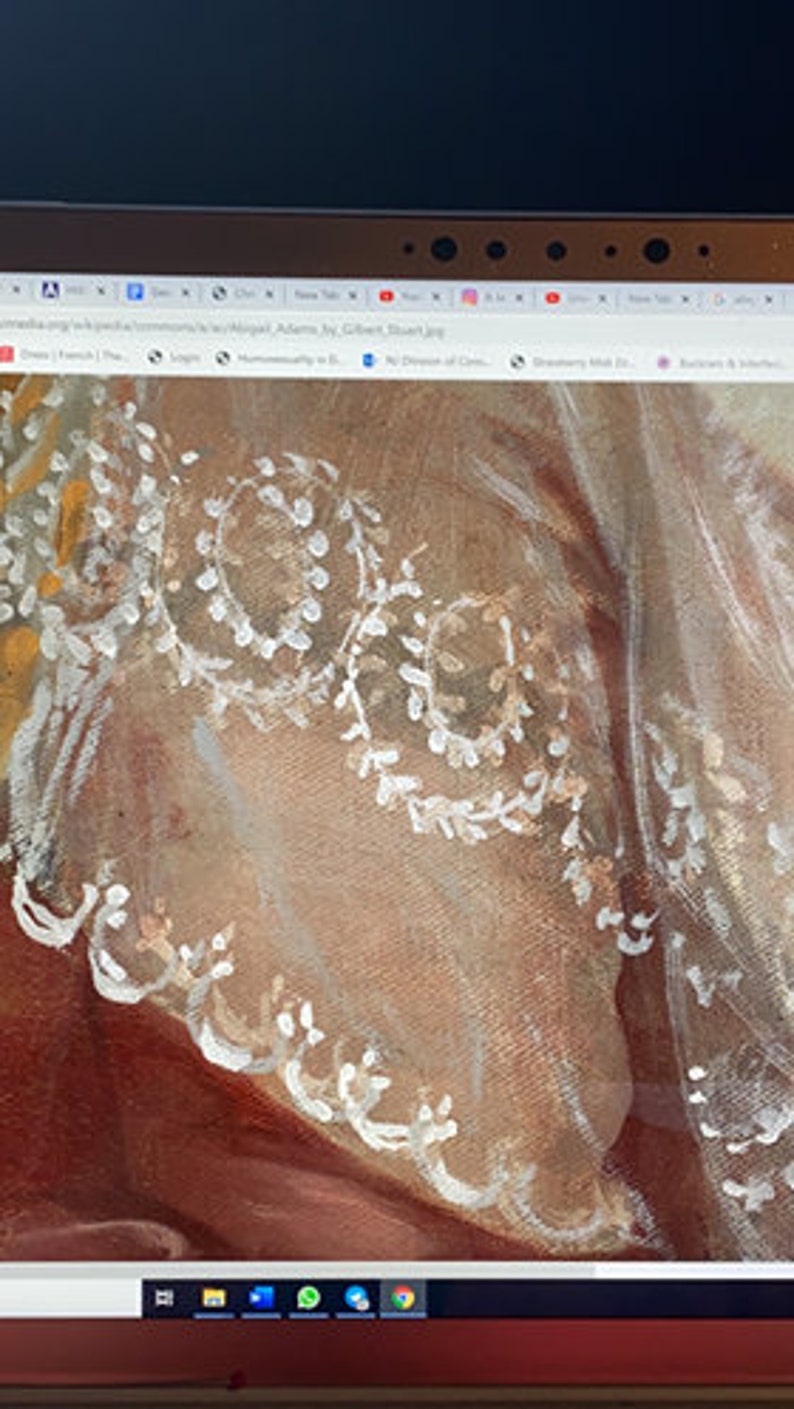 May include: Close-up of a white lace overlay on a brown fabric background. The lace has a delicate floral pattern with small white flowers and leaves.