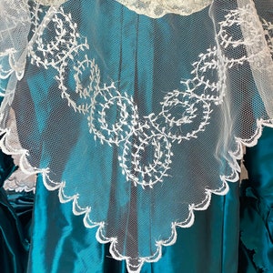 May include: A teal blue satin dress with a white lace overlay. The lace has a scalloped edge and a delicate floral pattern.