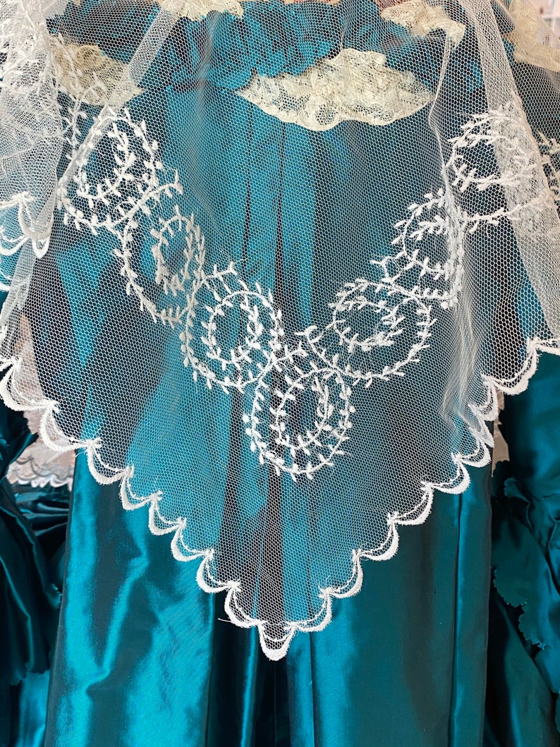 May include: A teal blue satin dress with a white lace overlay. The lace has a scalloped edge and a delicate floral pattern.