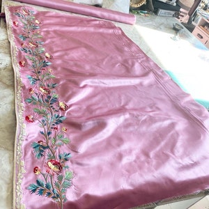 May include: Pink satin fabric with a floral embroidery design along the edge. The embroidery features pink, green, and white flowers.