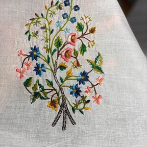 May include: White fabric with embroidered floral design featuring pink, blue, and yellow flowers with green leaves.
