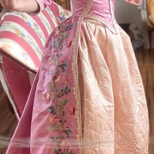 May include: A pink and cream silk dress with a floral embroidery design. The dress has a fitted bodice and a full skirt.