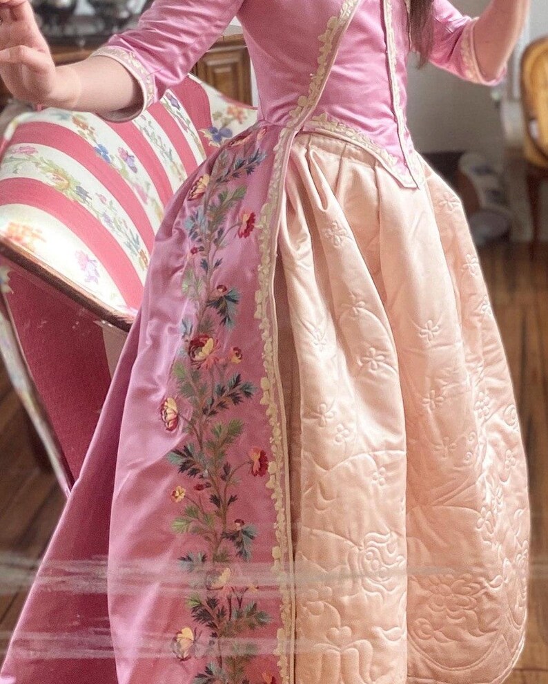 May include: A pink and cream silk dress with a floral embroidery design. The dress has a fitted bodice and a full skirt.