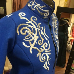 Könnte beinhalten: Eine blaue Jacke mit einem hohen Kragen und weißen Stickereien. Die Stickerei ist aufwendig und zeigt eine Vielzahl von wirbelnden Mustern.