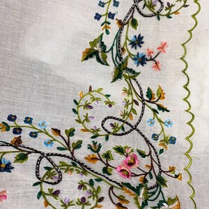 May include: White linen fabric with a green, brown, and silver embroidered floral design. The design features a vine with leaves, flowers, and a scalloped edge.