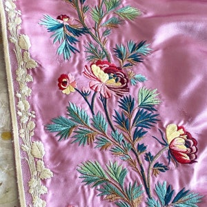 May include: Pink fabric with intricate embroidery of flowers and leaves in shades of green, red, and white. The embroidery is detailed and delicate, creating a beautiful floral pattern.