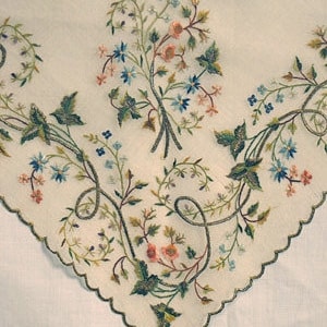 May include: A white linen handkerchief with delicate embroidered floral designs in shades of green, blue, and pink.
