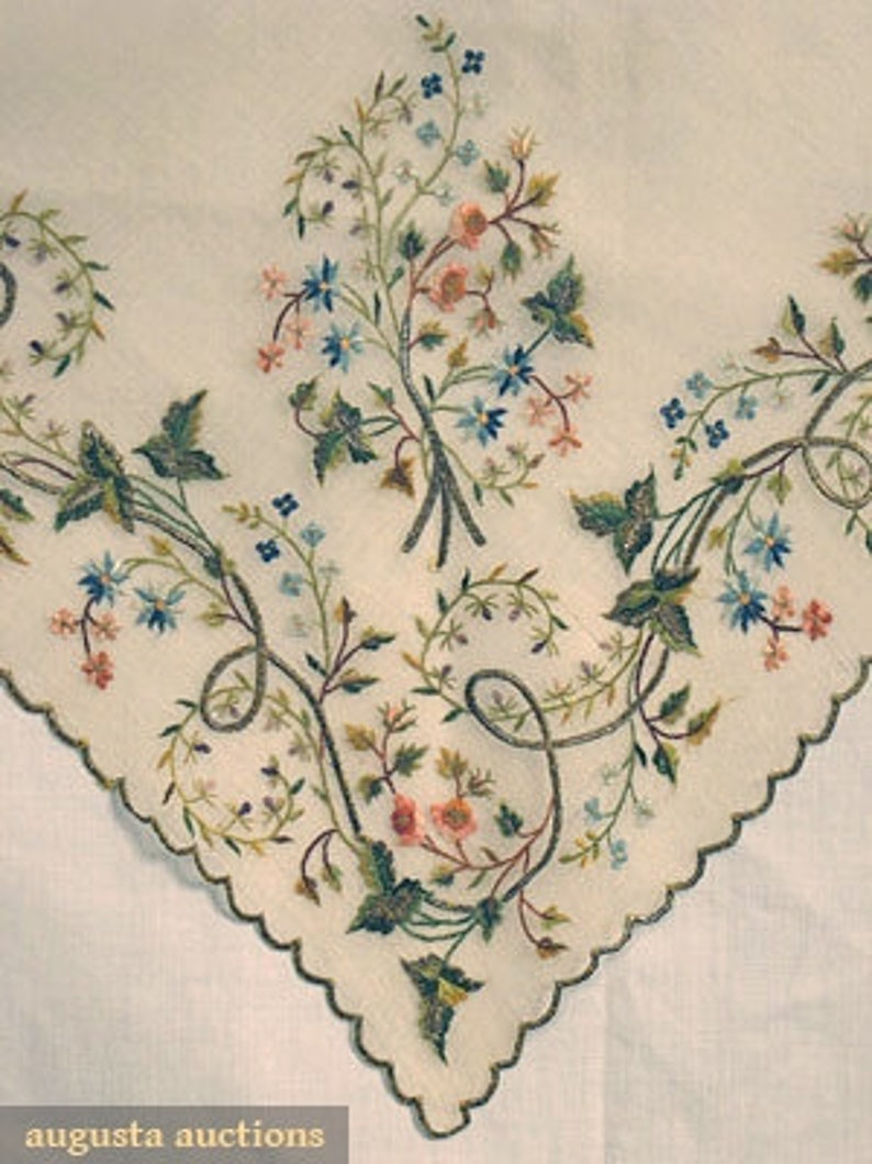 May include: A white linen handkerchief with delicate embroidered floral designs in shades of green, blue, and pink.