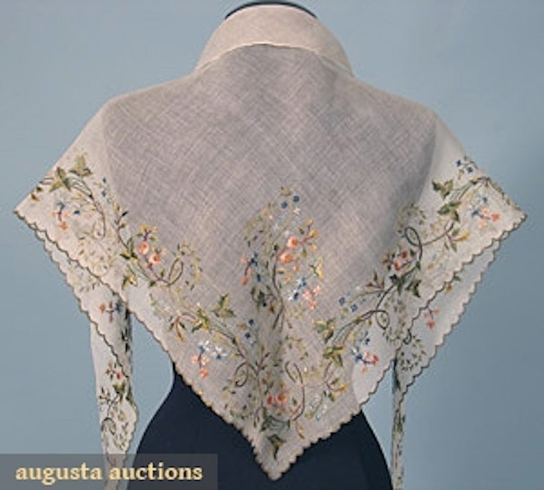 May include: A white linen scarf with a delicate floral embroidery design in shades of pink, blue, and green. The scarf has a scalloped edge and is trimmed with a white lace.