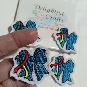 May include: Embroidered blue bow patches with red, yellow, and green ribbon accents. The patches have a white border. The text "Delightful Crafts" is visible in the background. Patches are on a white surface.