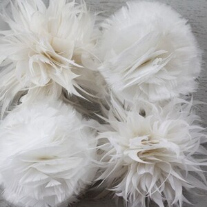 May include: Four white feather pom poms. The pom poms are made of soft, fluffy feathers and are perfect for adding a touch of elegance to any craft project.
