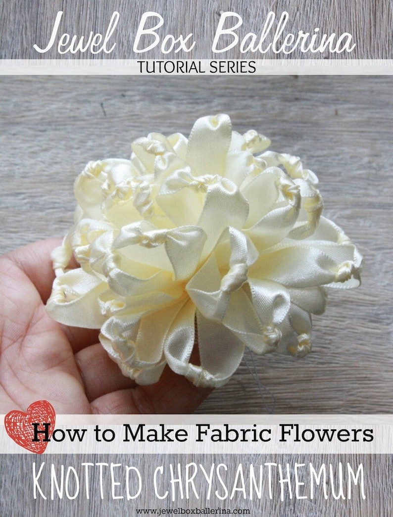K&ouml;nnte beinhalten: Nahaufnahme einer wei&szlig;en Stoffblume, die durch das Knoten von Band hergestellt wurde. Die Blume hei&szlig;t "Geknotete Chrysantheme" und ist Teil einer Tutorial-Serie namens "Jewel Box Ballerina".