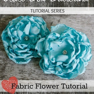 Könnte beinhalten: Eine Anleitung zum Herstellen einer fluffigen Rosenblüte aus Stoff. Das Bild zeigt zwei türkisfarbene Rosenblüten mit einer Strassverzierung in der Mitte jeder Blüte. Der Text auf dem Bild lautet "Jewel Box Ballerina Tutorial Series Fabric Flower Tutorial Fluffy Cabbage Rose www.jewelboxballerina.com"