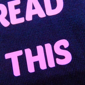 Op de afbeelding: Close-up van een donkerblauwe stof met de woorden "READ THIS" in roze.