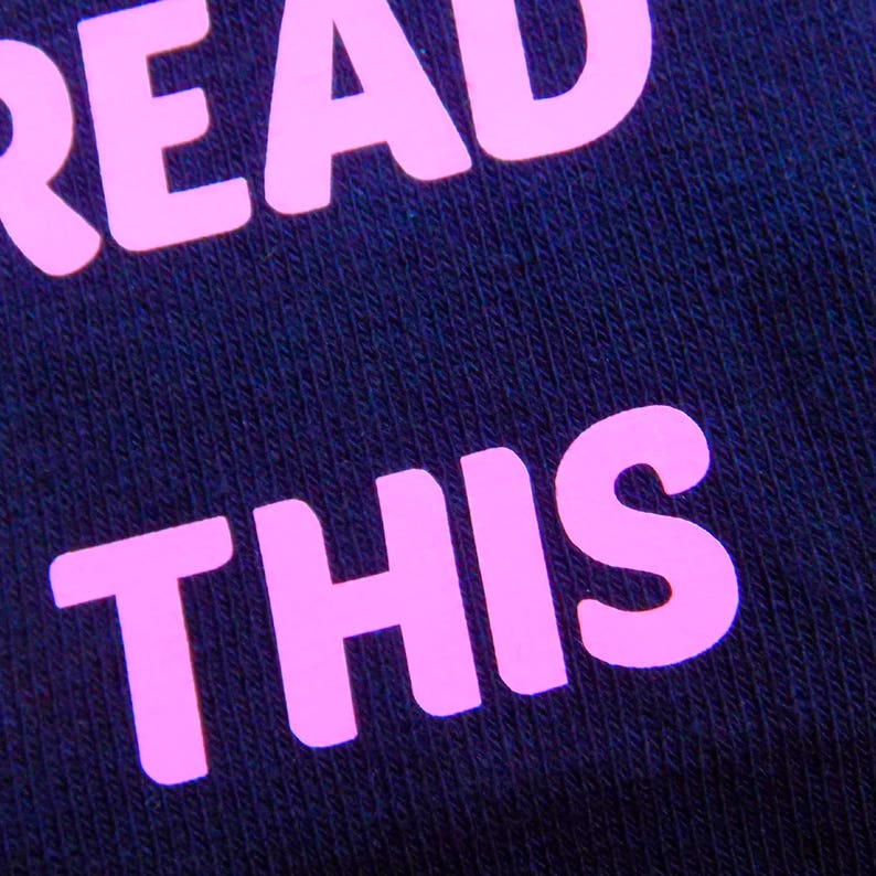 Op de afbeelding: Close-up van een donkerblauwe stof met de woorden "READ THIS" in roze.