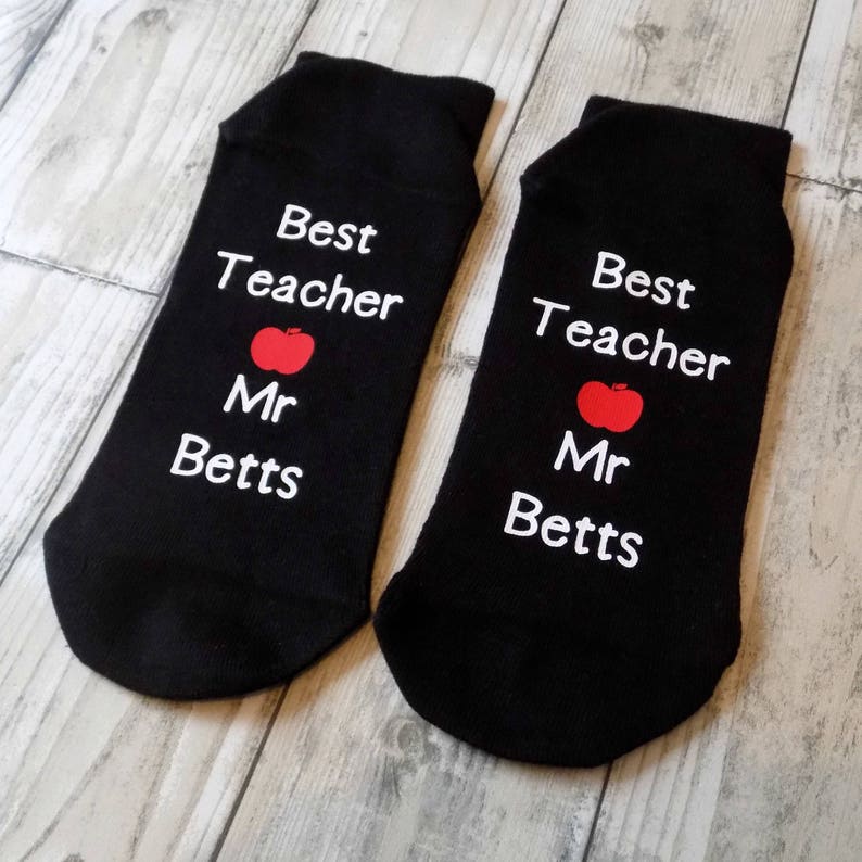 May include: A pair of black socks with white text that reads "Best Teacher Mr. Betts" and a red apple graphic.